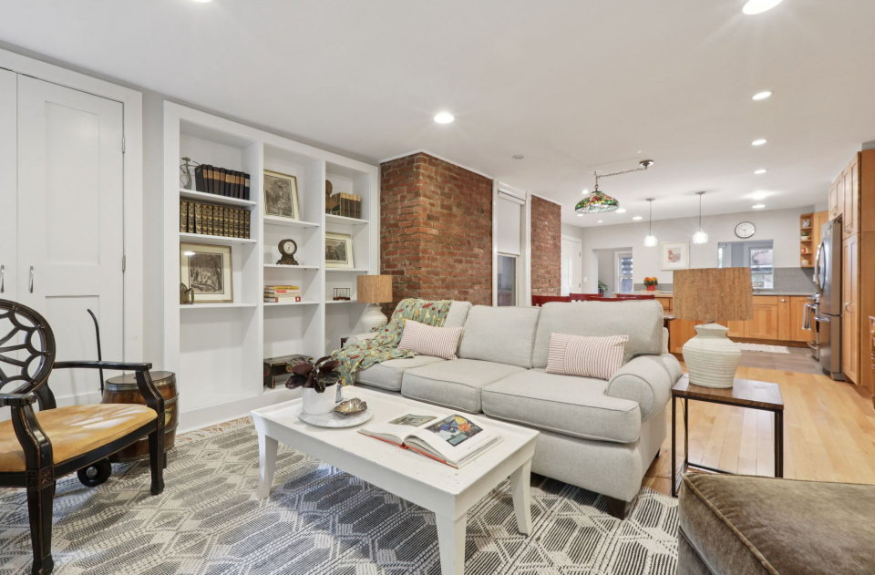 Staged open-concept living room with exposed brick and built-in shelves